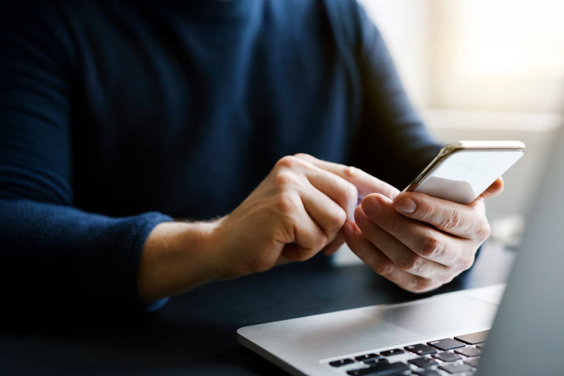man in blue shirt holding phone infront of computer